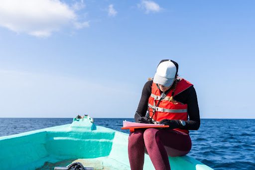 Marine biologist writing down data sitting on top of a boat in the middle of the sea