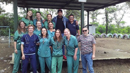 young people wearing green scrubs and stethoscopes outdoors at a rural medical facility